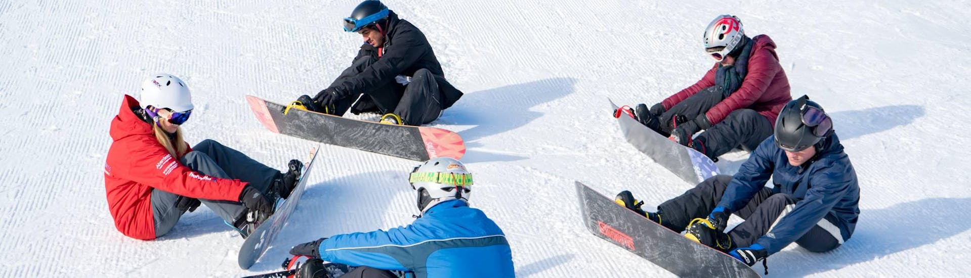 A group of snowboarders practise standing up at the snowboarding lessons for adults + snowboard rental for first timers with the Swiss Ski School Grindelwald.