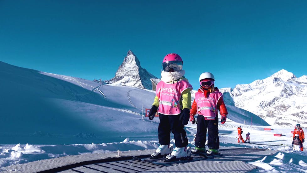 Two little girls are riding the magic carpet in the Snowli Kids Village Riffelberg during their Kids Ski Lessons (3-6 years) - Beginners with Zermatters.