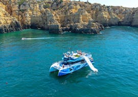 The boat used by Discover Tours Lagos for the Catamaran Trip around Lagos with Dolphin Watching in a secluded bay where kids are swimming in the blue water.