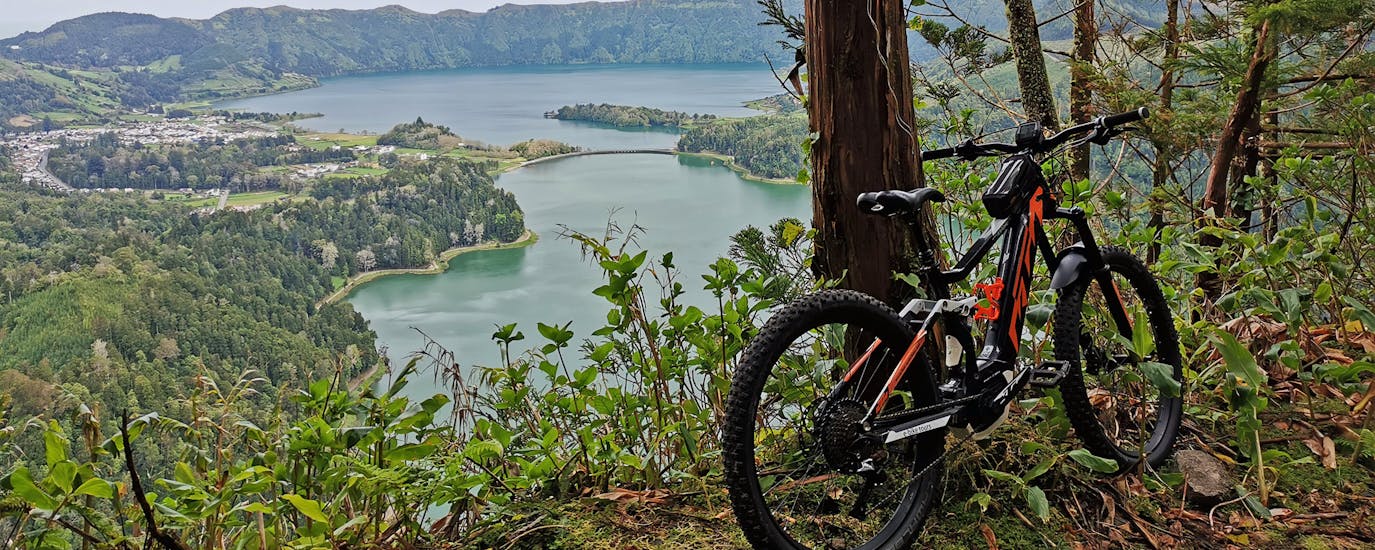 A bike leaning on a tree in front of a great view of blue lagoon during a E-Bike Self Guided tour in Sete Cidades with Fun Activities Azores Adventures.