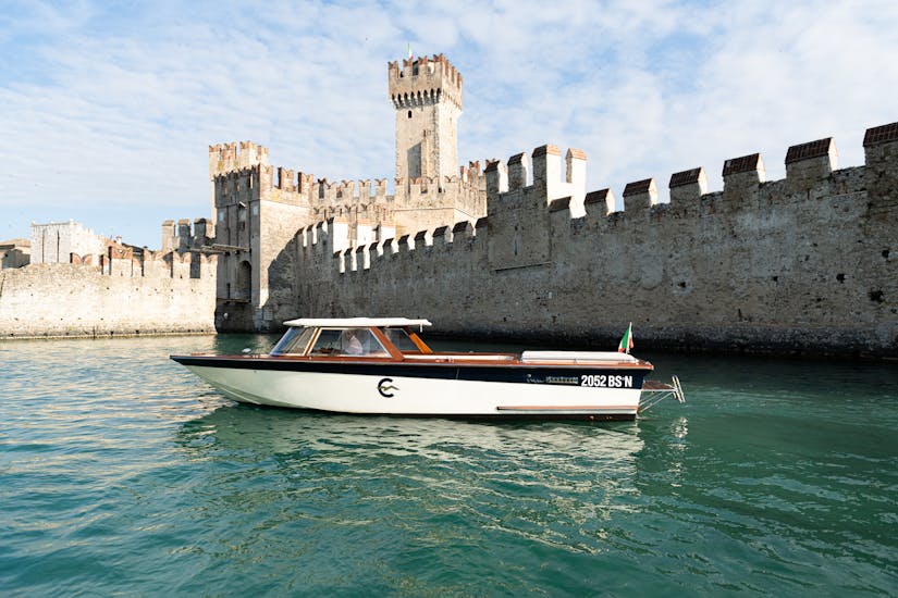 Un barco de madera de estilo veneciano frente a las murallas del castillo Scaliger de Sirmione utilizado durante el paseo en barco privado por el lago de Garda con Consolini Boats.