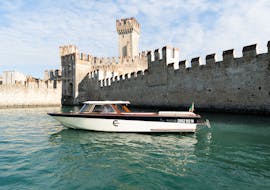 A Venetian-style wooden boat in front of the walls of the Scaliger castle in Sirmione used during the private boat trip on Lake Garda with Consolini Boats.