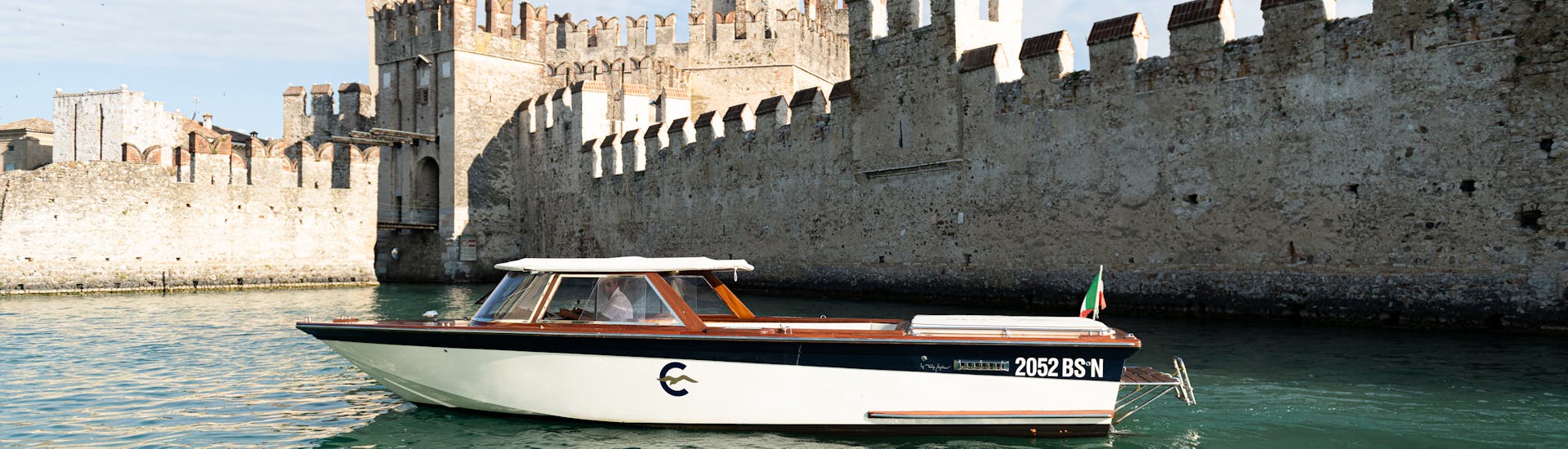 Un'imbarcazione in legno in stile veneziano davanti alle mura del castello scaligero di Sirmione, utilizzata durante la gita privata in barca sul Lago di Garda con Consolini Boats.