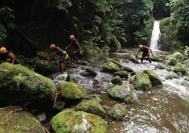 Group of people jumping over stones to cross a river while Canyoning Ribeira da Salga Half Day with Fun Activities Azores Adventures.