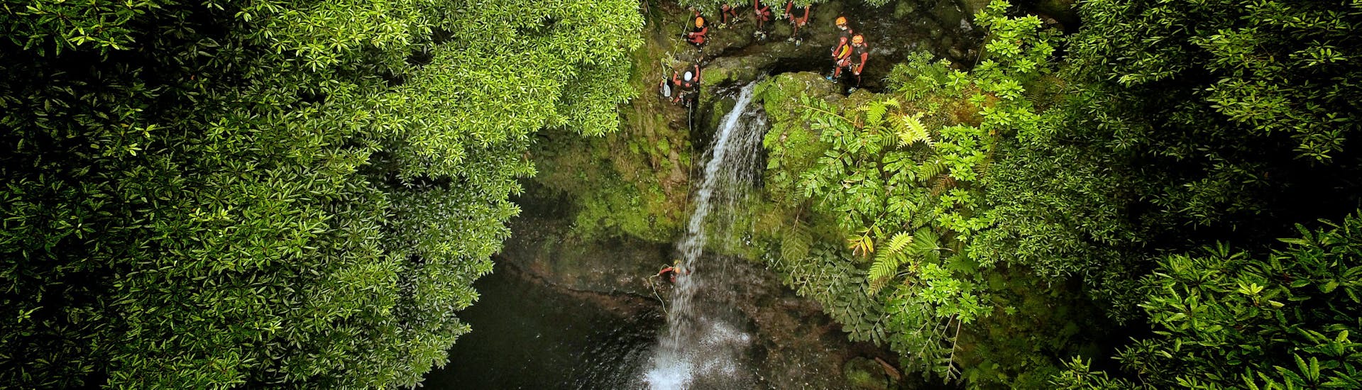 Eine Gruppe von Leuten springt einen Wasserfall hinunter während des Canyoning Ribeira da Salga Halbtages mit Fun Activities Azores Adventures.