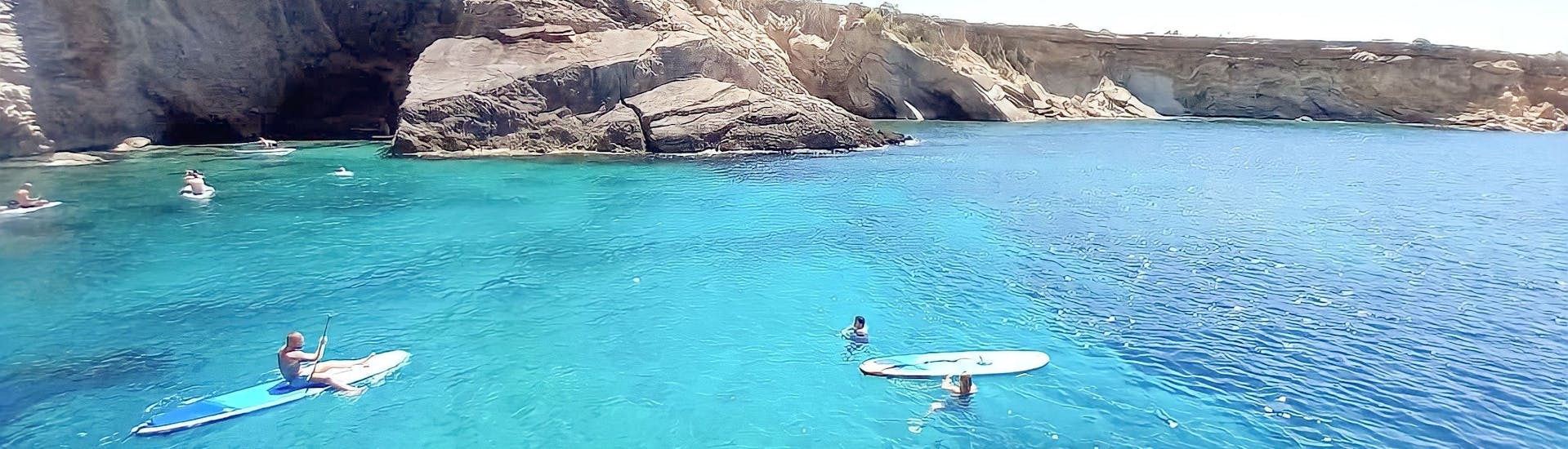 Aguas Turquesas en la costa de Ibiza y algunas personas disfrutando de actividades de agua con un barco privado de Salvador Ibiza.