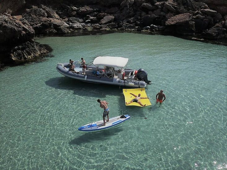 Barca con persone nell'acqua di una baia che praticano stand-up paddling, snorkeling e nuoto durante la gita in barca a Ibiza con snorkeling e open bar di Arenal Diving & Boat Trips Ibiza.