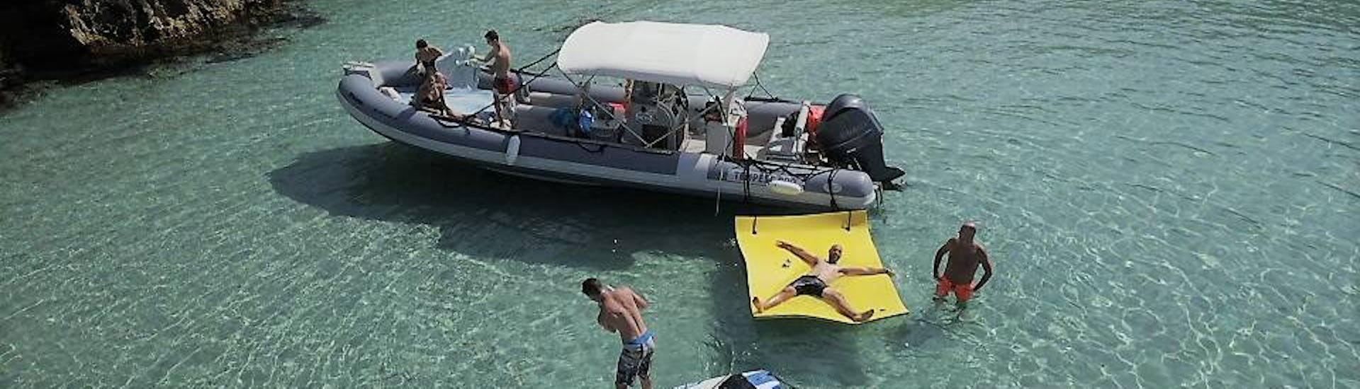 Barca con persone nell'acqua di una baia che praticano stand-up paddling, snorkeling e nuoto durante la gita in barca a Ibiza con snorkeling e open bar di Arenal Diving & Boat Trips Ibiza.