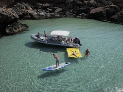 Boat with people in the water of a cove doing standup paddling, snorkeling and swimming during Private Boat Trip in ibiza with Snorkeling and Open Bar by Arenal diving.