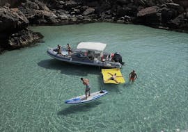 Boot met mensen in het water van een baai die standup paddling, snorkelen en zwemmen doen tijdens Privée Boottocht in ibiza met Snorkelen en Open Bar door Arenal diving.