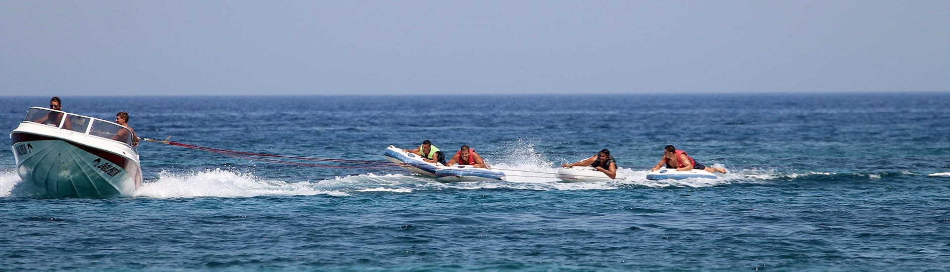 Las personas en los deslizadores se esfuerzan durante la actividad Banana Boat y otros hinchables en la playa de Malia con Dolphin Water Sports.