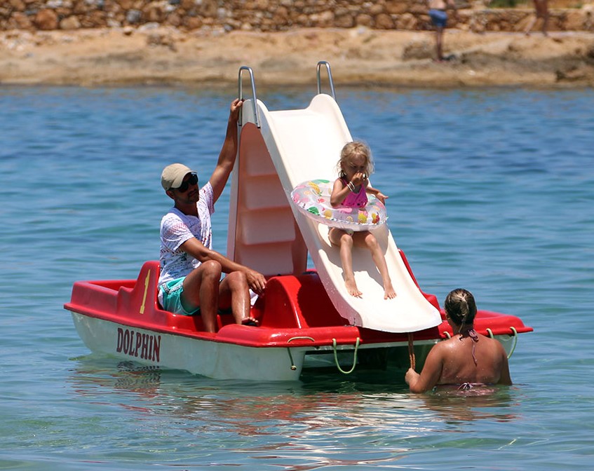 A father helps his young girl to use the slide during the Pedal Boat at Malia beach in Crete with Dolphin Water Sports.
