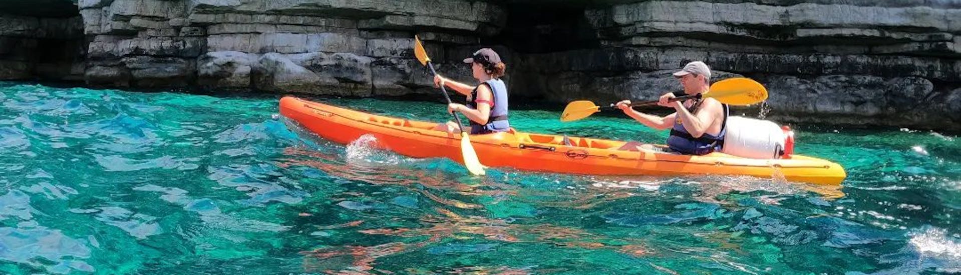 Kayak da mare nelle acque blu dell'Adriatico davanti a una grotta durante l'escursione in kayak da mare alle grotte di Pola del Pula Adventure Team.