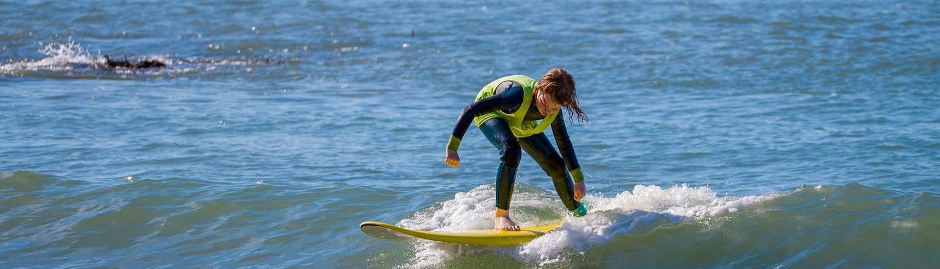 A kid is doing his first steps on a surf board thanks to our Private Surf Lessons (from 12 y.) for All Levels in Ericeira with Activity Surf Center Ericeira.