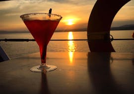 Cocktail rosso su un tavolo con un bellissimo tramonto della Calcidica durante il giro in barca dell'isola di Ammouliani con le crociere giornaliere e private di Eirinikos Glassbottom.