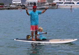 A dad and his young kid having fun on the SUP during the SUP Hire at Ammoudi Beach in Agios Nikolaos with Amoudi Watersports.