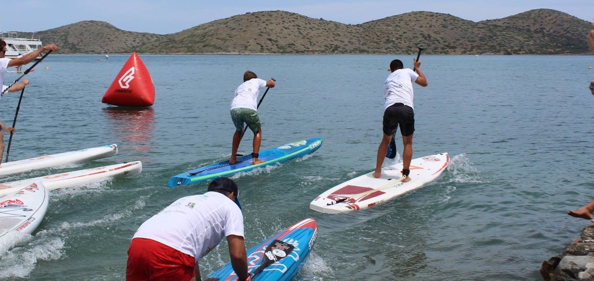 People are doing a race and paddle with all their strength during the SUP Hire at Ammoudi Beach in Agios Nikolaos with Amoudi Watersports.