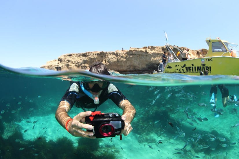 Boy with a camera under water doing snorkeling surrounded by a lot of fish during Snorkeling in Ses Salines Natural Park from Formentera by Vellmari Diving Center Formentera.