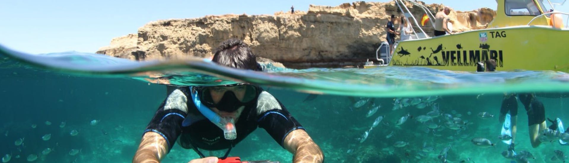 Ragazzo con macchina fotografica sott'acqua mentre fa snorkeling circondato da molti pesci durante lo Snorkeling nel Parco Naturale di Ses Salines di Formentera a cura del Vellmari Diving Center Formentera.