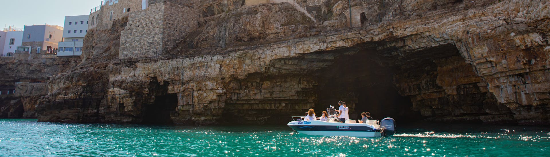 La barca di Blue Wave che costeggia le grotte di Polignano a Mare durante il Giro in barca alle grotte di Polignano a Mare con aperitivo con Blue Wave.