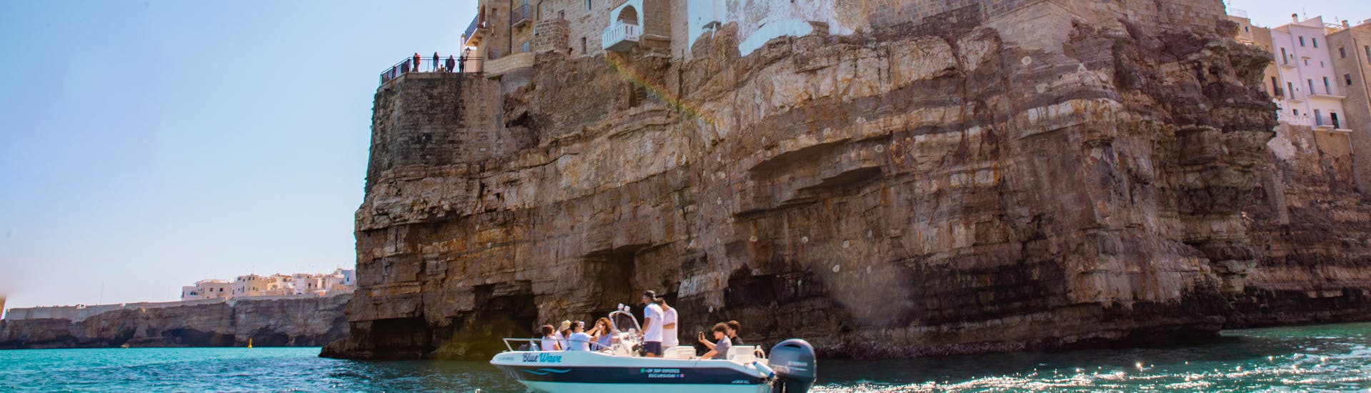 La barca di Blue Wave che costeggia Polignano a Mare durante la gita in barca alle grotte di Polignano a Mare con aperitivo con Blue Wave.