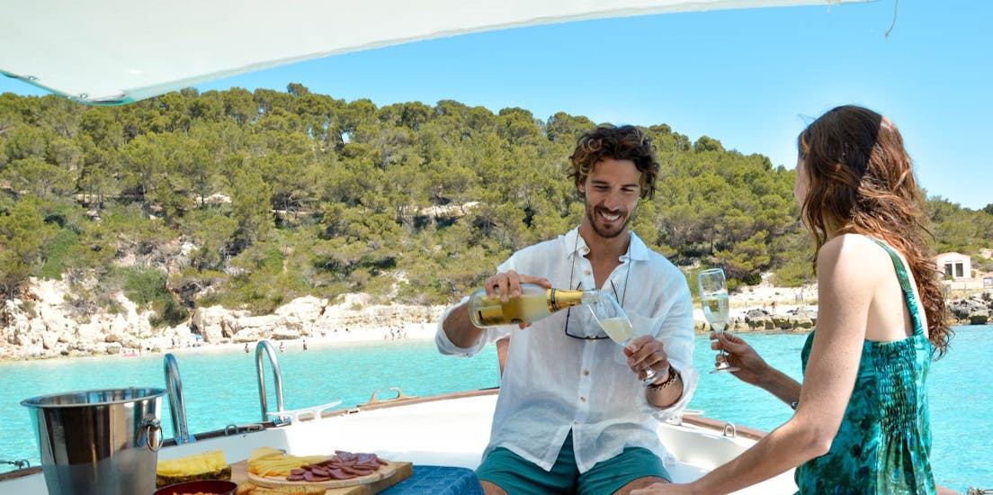 Hombre y mujer bebiendo champán en el paseo en barco privado de Cala Galdana a Cala en Turqueta con aperitivo y buceo.