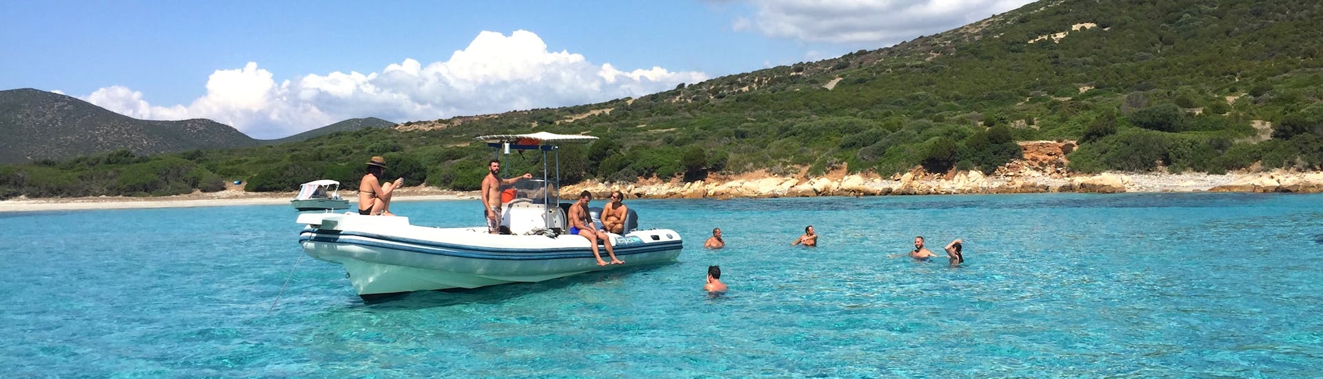 Teilnehmer schwimmen in einer klaren Bucht um das Boot während der Privaten RIB-Bootstour von Cagliari zum Strand von Mari Pintau mit Schnorcheln.