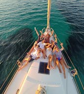 Mensen vermaken zich tijdens de privé zeiltocht bij zonsondergang rond Alghero met aperitief met Cruise Sail Charter Alghero.