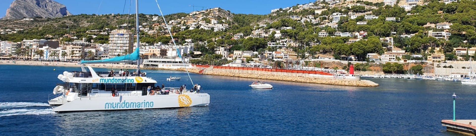 Uno dei catamarani di Mundo Marino Valencia naviga lungo la costa durante una festa in catamarano con DJ e bicchiere di cava di benvenuto.