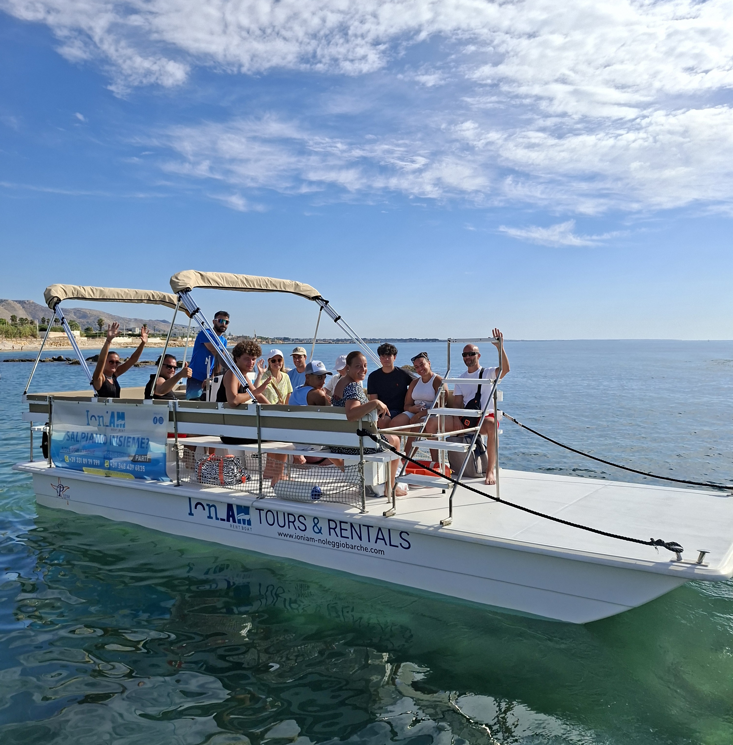 Happy guests wave from the deck of a boat during a trip from Avola to Marzamemi with swimming stops and snorkeling, provided by Ioniam Rent Boat Avola.