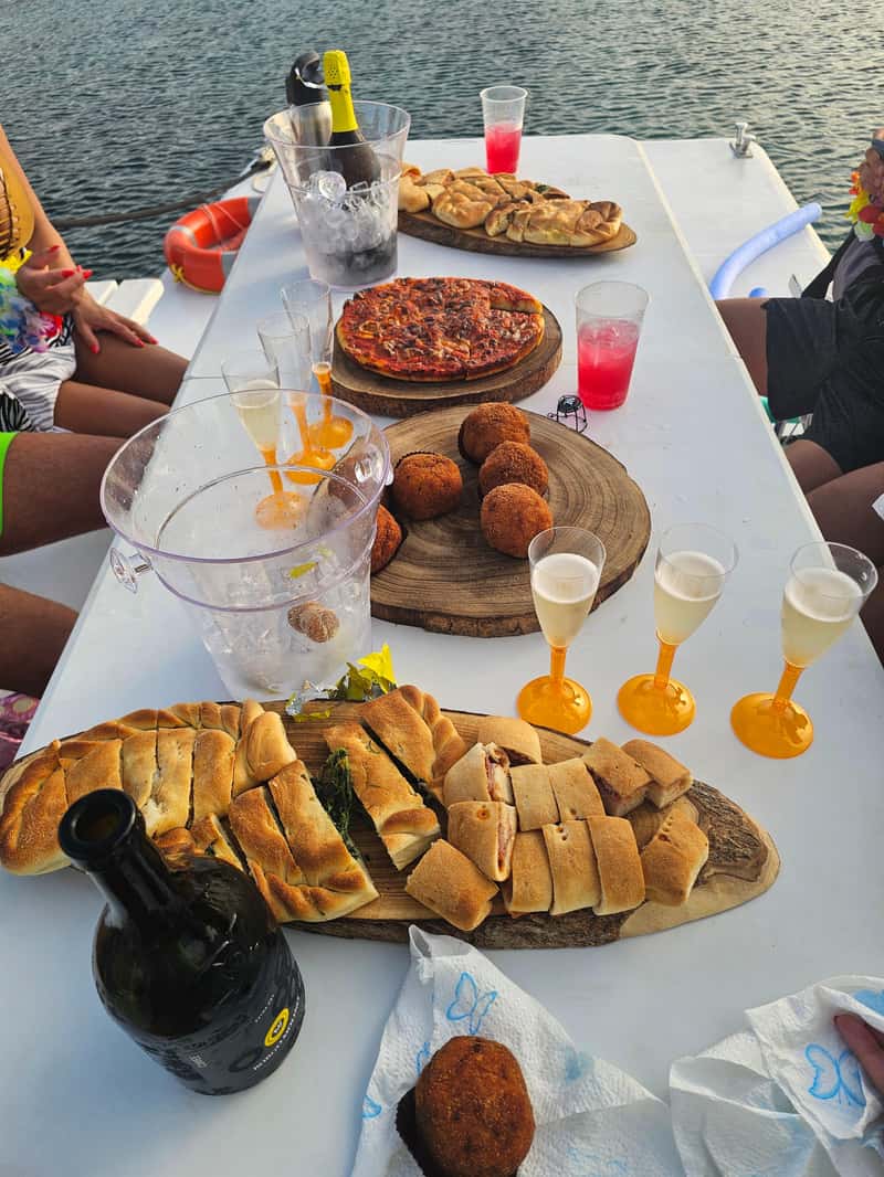 Huéspedes disfrutando de un aperitivo en un paseo en barco. Durante una excursión en barco desde Avola a Marzamemi, con paradas para nadar y practicar snorkel, se sirve un exquisito aperitivo con pizza, especialidades locales y prosecco a cargo de Ioniam Rent Boat Avola.