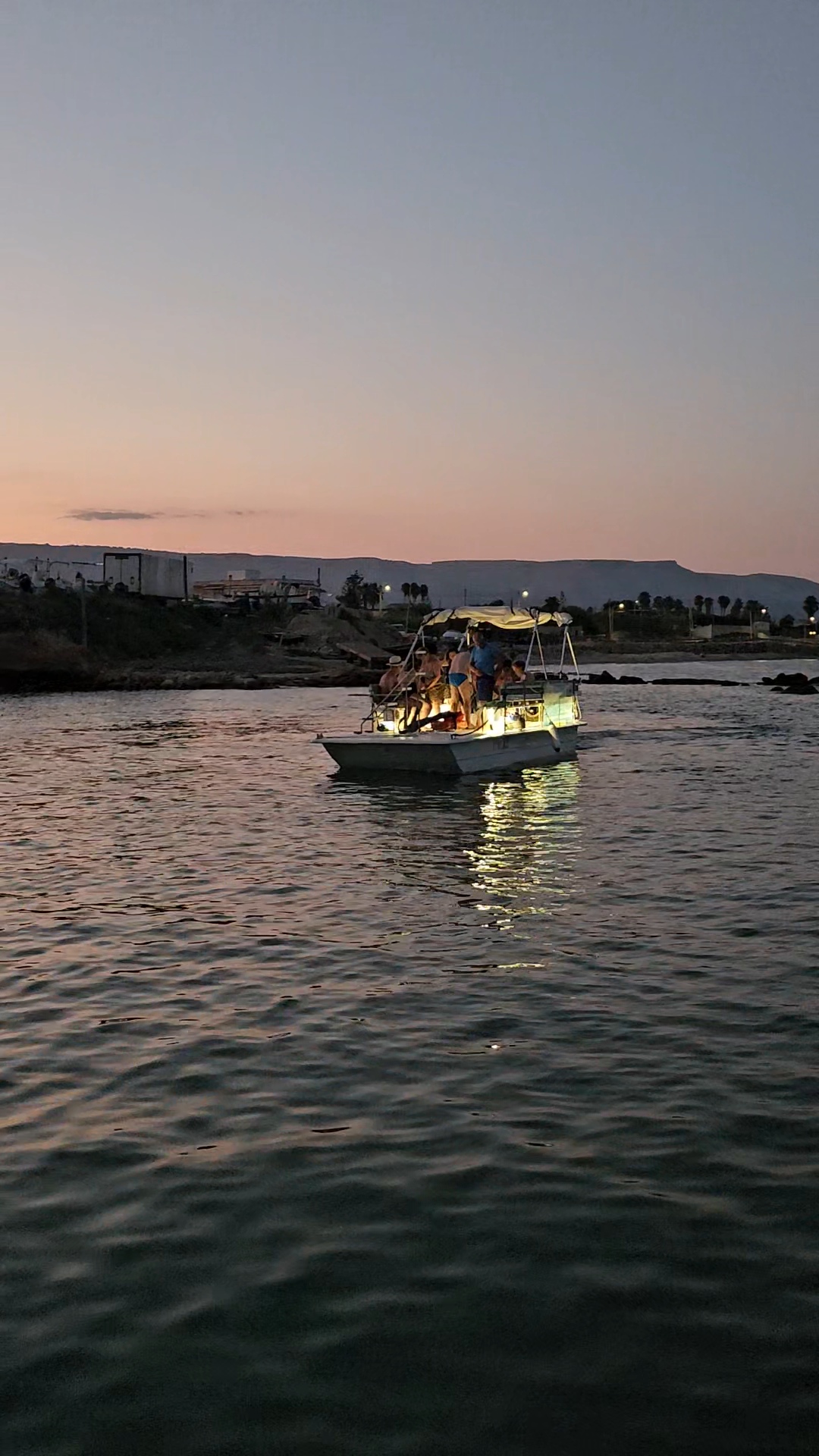 Gruppo di persone in gita in barca al tramonto Un gruppo di persone si gode una serata su una barca illuminata durante l'escursione in barca al tramonto da Avola a Marzamemi con aperitivo, offerta da Ioniam Rent Boat Avola.
