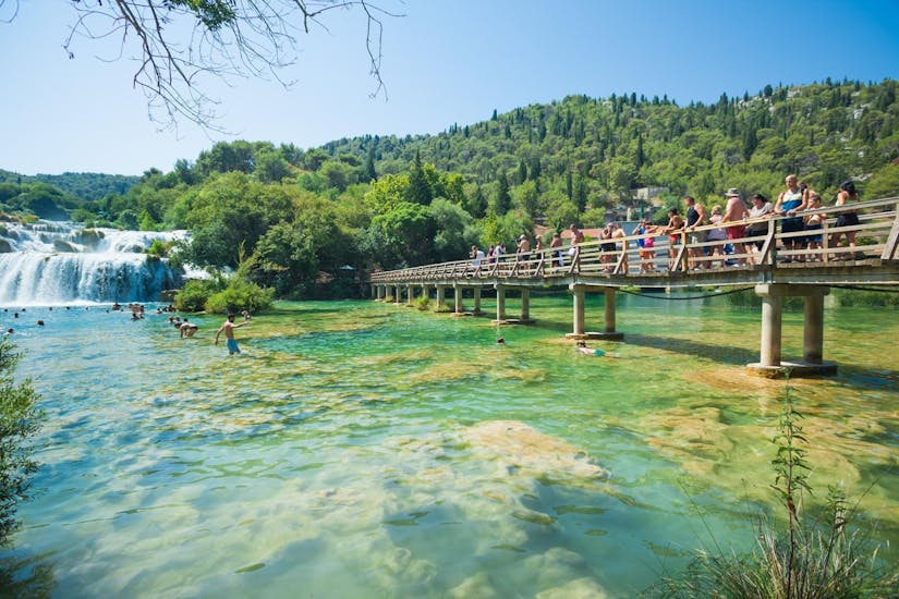 People walking on a wooden trail across one of the lakes during the Bus & Boat Trip to Krka National Park and Primošten with Swimming with Splitlicious Experiences.
