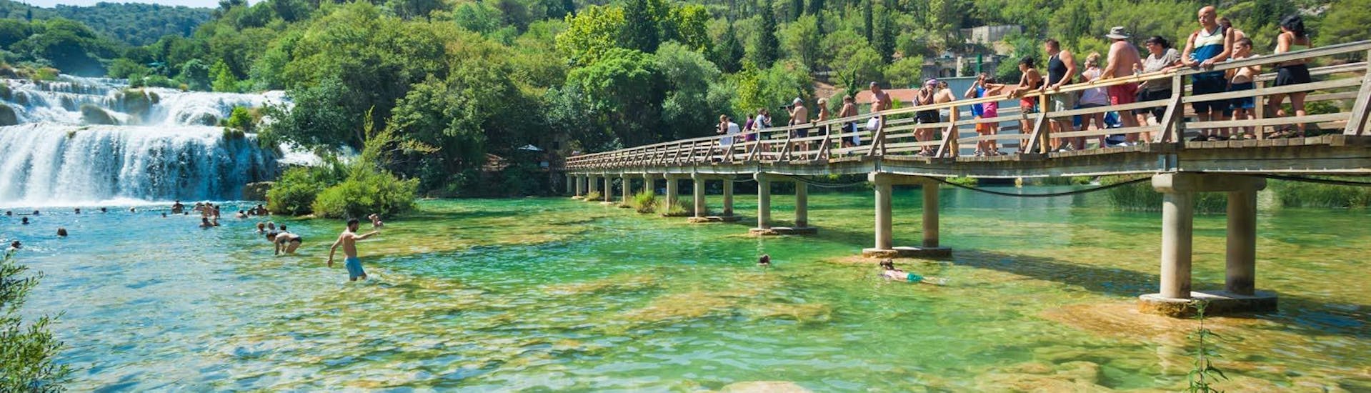 Gruppe, die auf einem Holzsteg über einen der Seen während der Bus- & Bootstour zum Krka Nationalpark und Primošten mit Schwimmen mit Splitlicious Experiences geht.
