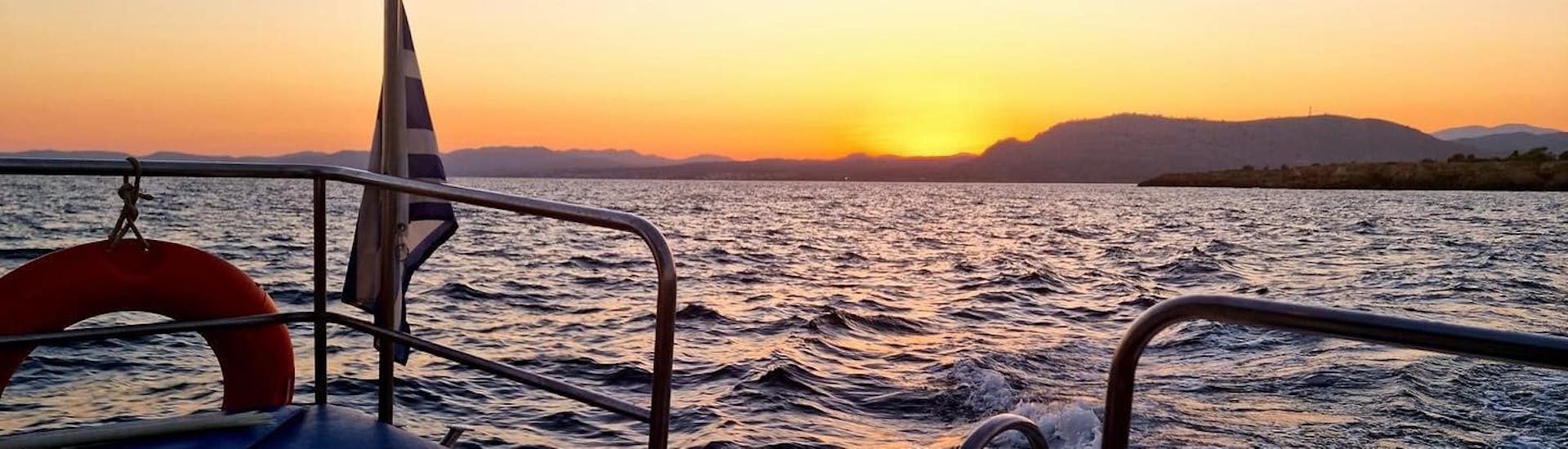 El barco navega bajo la puesta de sol durante Paseo privado en barco con fondo de cristal al atardecer desde Lindos con baño en la bahía de Navarone