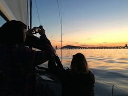 Personas haciendo fotos al atardecer durante un paseo en barco velero por Barcelona con barra libre de Cava al atardecer con Barcelona Sailboats.