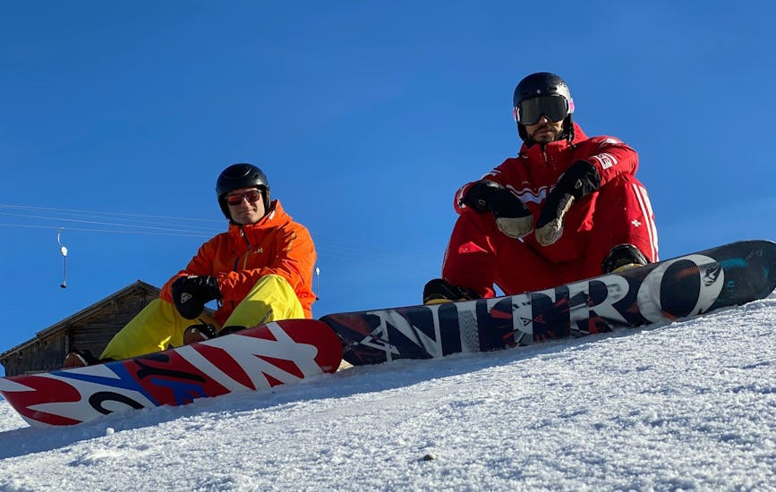 Ein Snowboardlehrer und ein Schüler sitzen im Schnee während dem Privaten Snowboardkurs für Kinder & Erwachsene aller Levels.