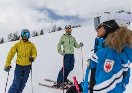 Zwei Erwachsene auf der Piste im Gespräch mit dem Skilehrer.