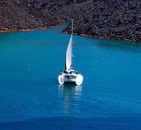 A catamaran on the blue sea of the Aegean Sea during the Private Morning Catamaran Trip along the Caldera with BBQ & Open Bar from Volcano Yachting Santorini.