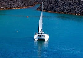 A catamaran on the blue sea of the Aegean Sea during the Private Morning Catamaran Trip along the Caldera with BBQ & Open Bar from Volcano Yachting Santorini.