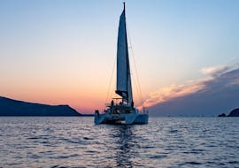 A catamaran with the colorful backdrop of the sunset during the Private Sunset Catamaran Trip along the Caldera with BBQ & Open Bar from Volcano Yachting Santorini.