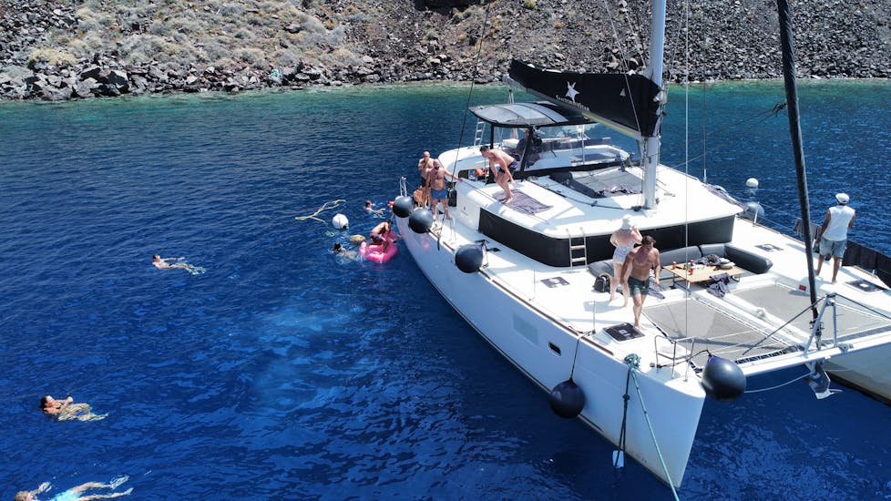 Un grupo se baña en la costa durante un Paseo en catamarán por la costa de Santorini con almuerzo y baño con Santorini Sailing Star Luxury.