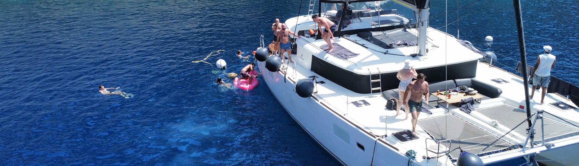 Un grupo se baña en la costa durante un Paseo en catamarán por la costa de Santorini con almuerzo y baño con Santorini Sailing Star Luxury.