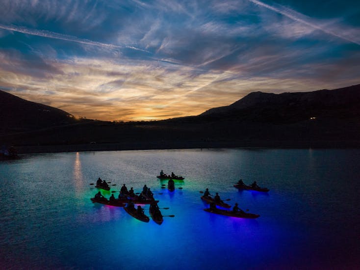 Mensen kajakken met een mooi uitzicht en met kleurrijke lichtjes onder zich tijdens de Nacht Glow kajaktocht in de baai van Pag vanaf het strand van Ručica.