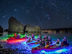 Groep mensen in de kajak met de lichten eronder tijdens de Nacht Glow kajaktocht in de baai van Pag vanaf het strand van Ručica met Sunturist.