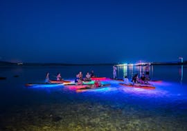 Mensen ontspannen op hun SUP boards met de kleurrijke verlichting tijdens de Nacht Glow SUP Tour naar Zrće Strand en Tunera met Sunturist.