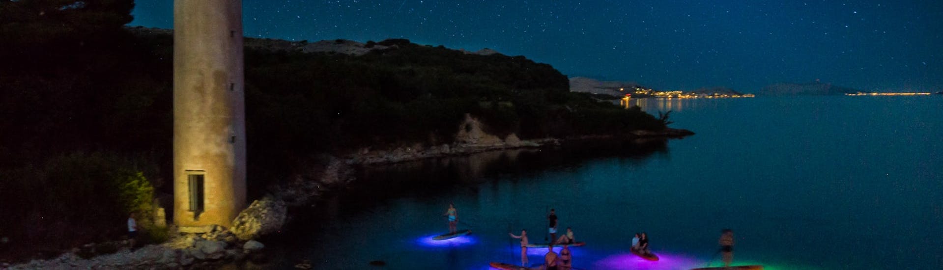 People peddling on their colourful SUPS nearby the Tunera Tower during the Night Glow SUP Tour to Zrće Beach and Tunera from Sunturist Novalja.