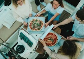 Un grupo de amigos disfruta de una cena durante Paseo privado en barco de vela en Barcelona con pizza y bebidas con Vela Boat Trips Barcelona.
