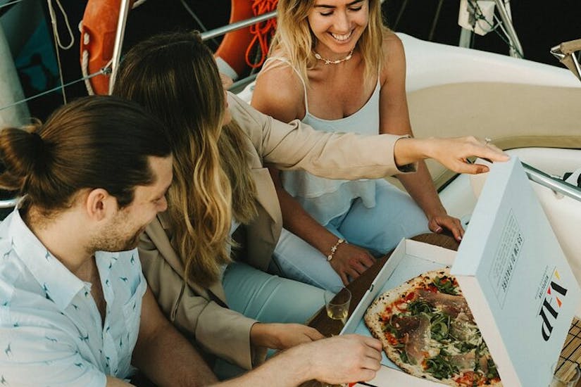 Un grupo de amigos disfruta de una pizza durante un Paseo privado en barco de vela en Barcelona con pizza y bebidas.
