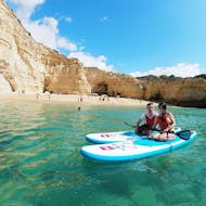A couple on SUPs in front of a beautiful beach during the SUP Tour to the Benagil Cave from Blue Xperiences Algarve.